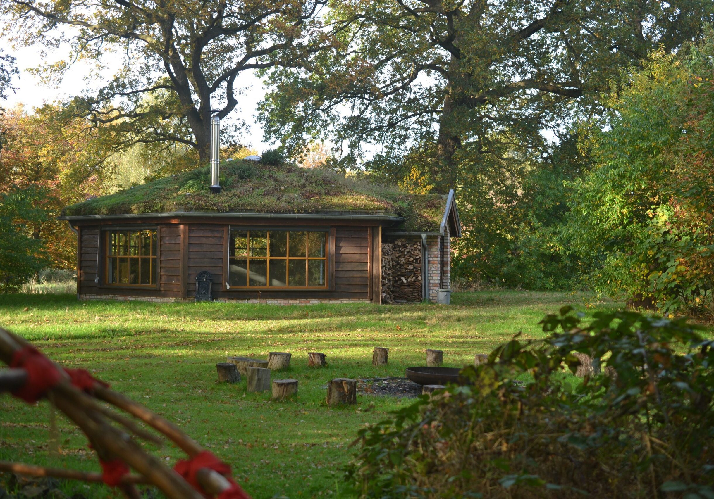 De natuurtempel van de buitenkant, omringd door grote eikenbomen en met een groen dak.